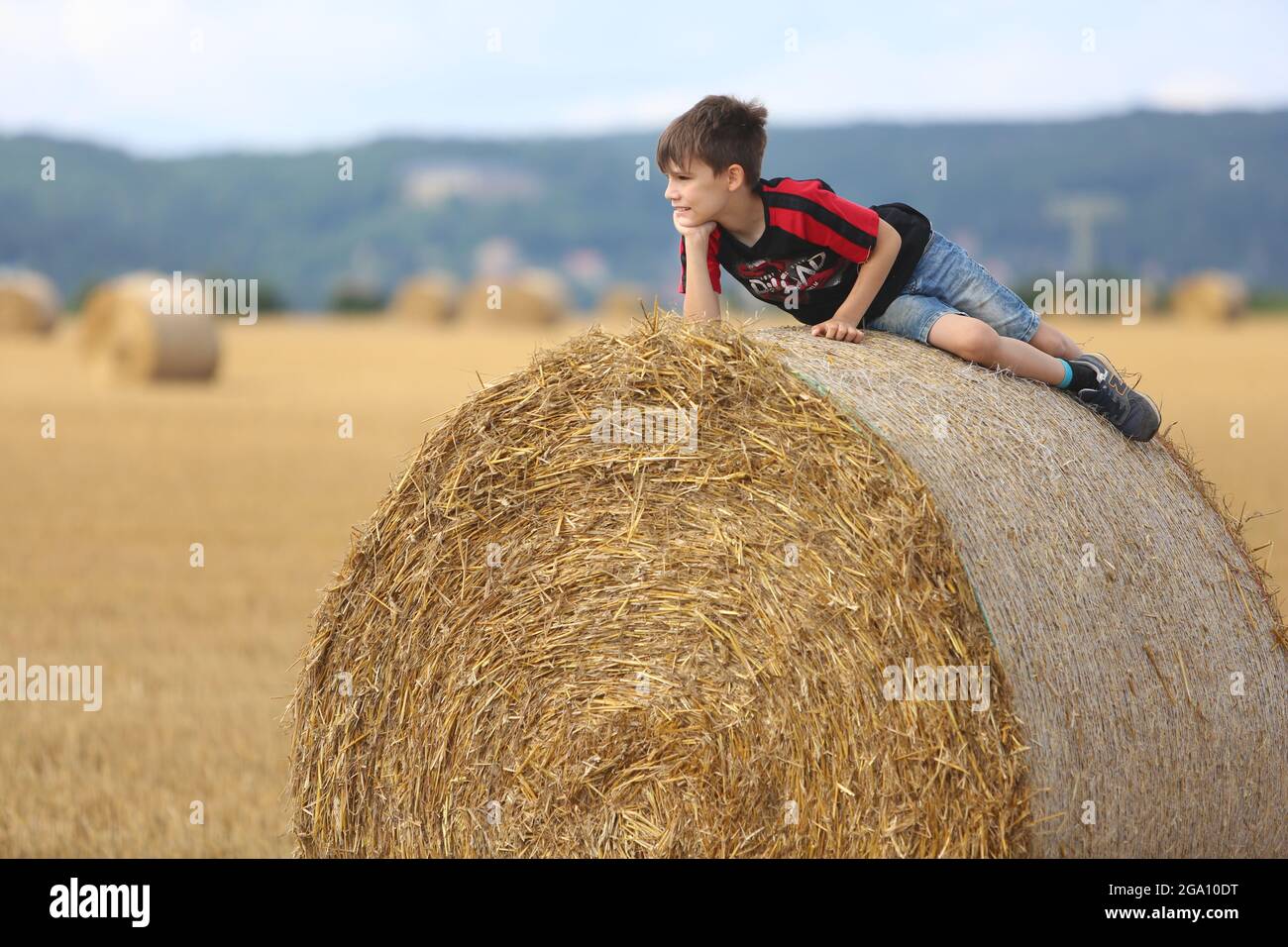 Blankenburg, Deutschland. Juli 2021. Strohballen liegen auf einem Feld im Vorland des Harzes. Ein kleiner Junge ruht auf den schweren Rollen und genießt das freundliche warme Wetter. Quelle: Matthias Bein/dpa-Zentralbild/ZB/dpa/Alamy Live News Stockfoto