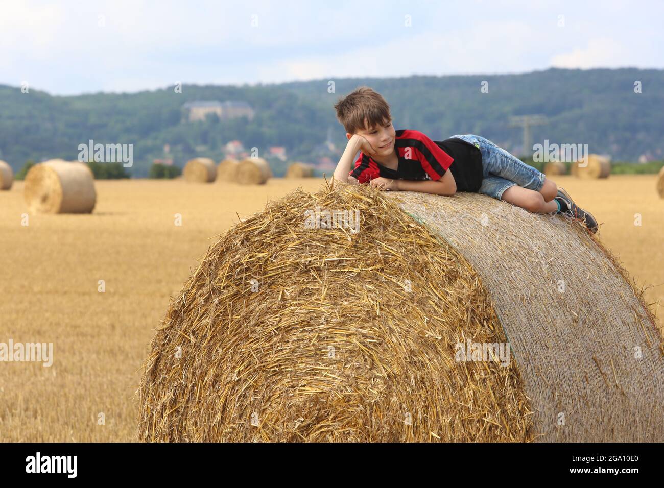 Blankenburg, Deutschland. Juli 2021. Strohballen liegen auf einem Feld im Vorland des Harzes. Ein kleiner Junge ruht auf den schweren Rollen und genießt das freundliche warme Wetter. Quelle: Matthias Bein/dpa-Zentralbild/ZB/dpa/Alamy Live News Stockfoto