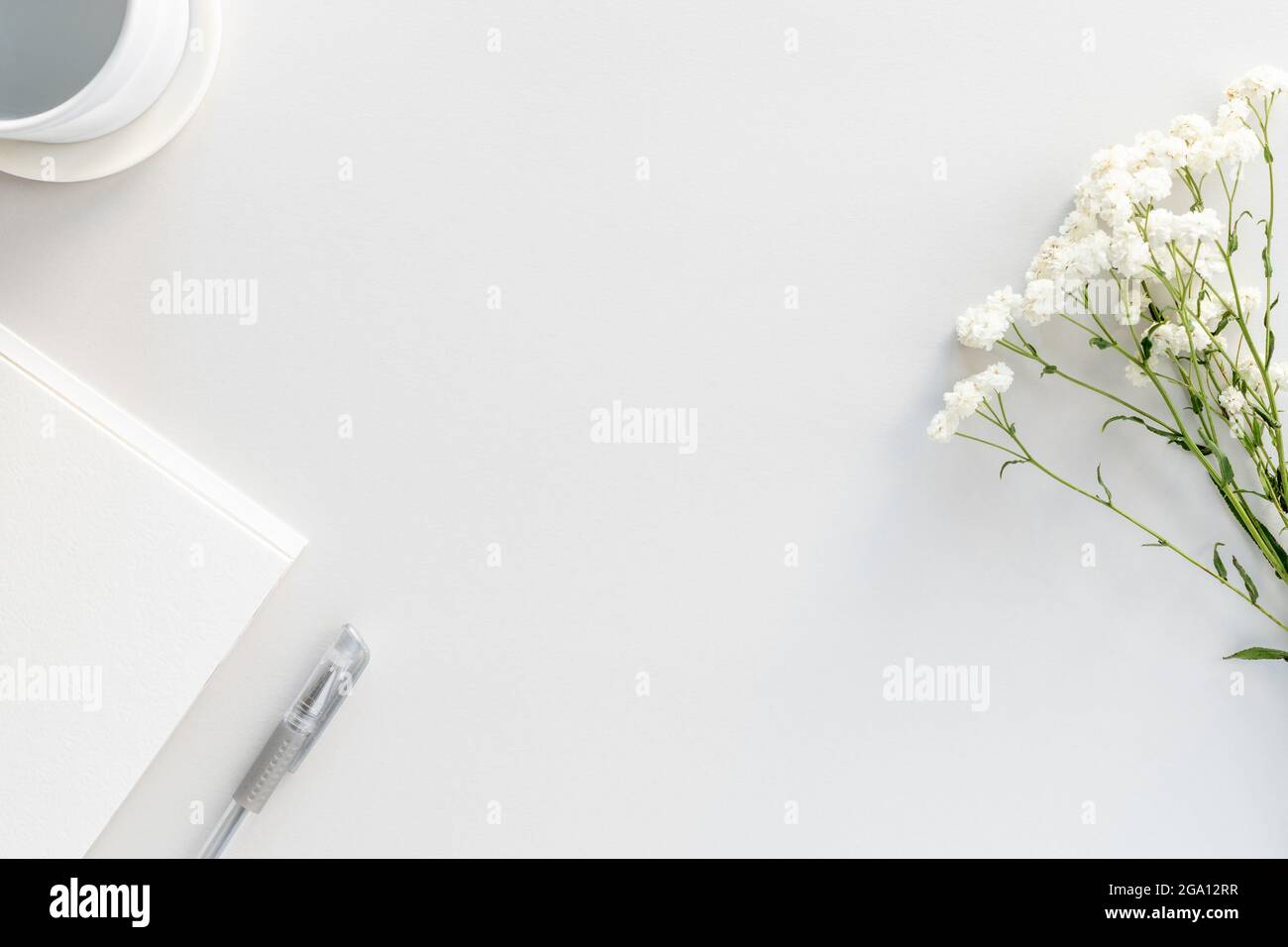 Flacher Arbeitstisch mit Notizblock aus Papier, Stift, reinem Wasser und Gipsophila-Blüten Stockfoto