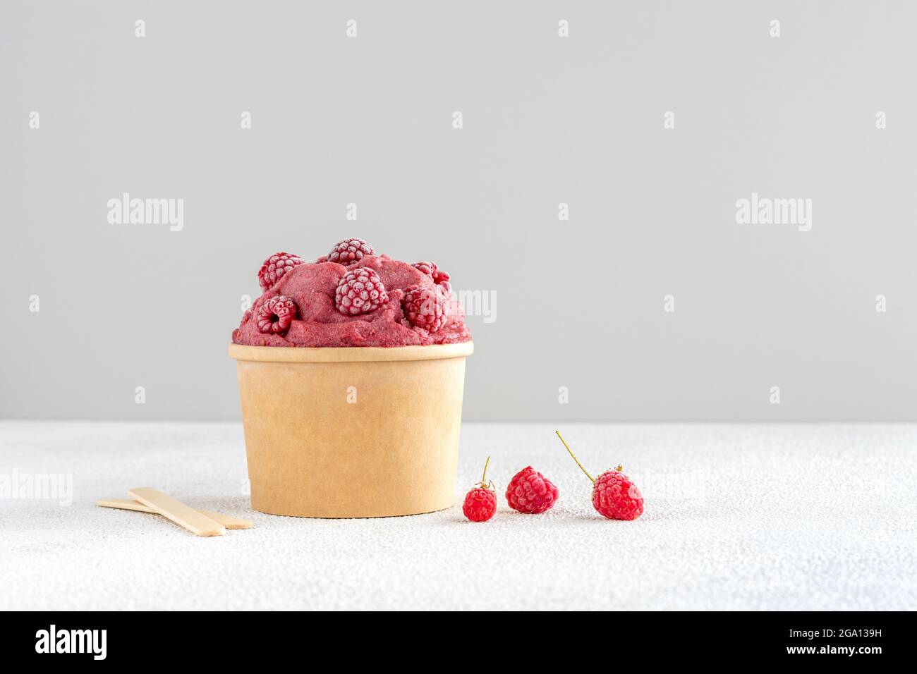 Rote Himbeere und Banane veganes Eis mit gefrorenen Himbeeren in Papierschüssel Stockfoto