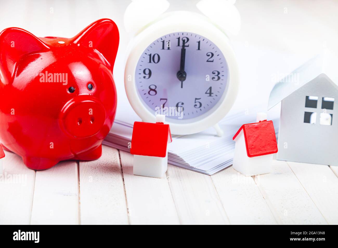 Schweinebank und kleine Häuser auf dem Hintergrund der Uhr. Zeit, um für Immobilien zu sparen. Stockfoto