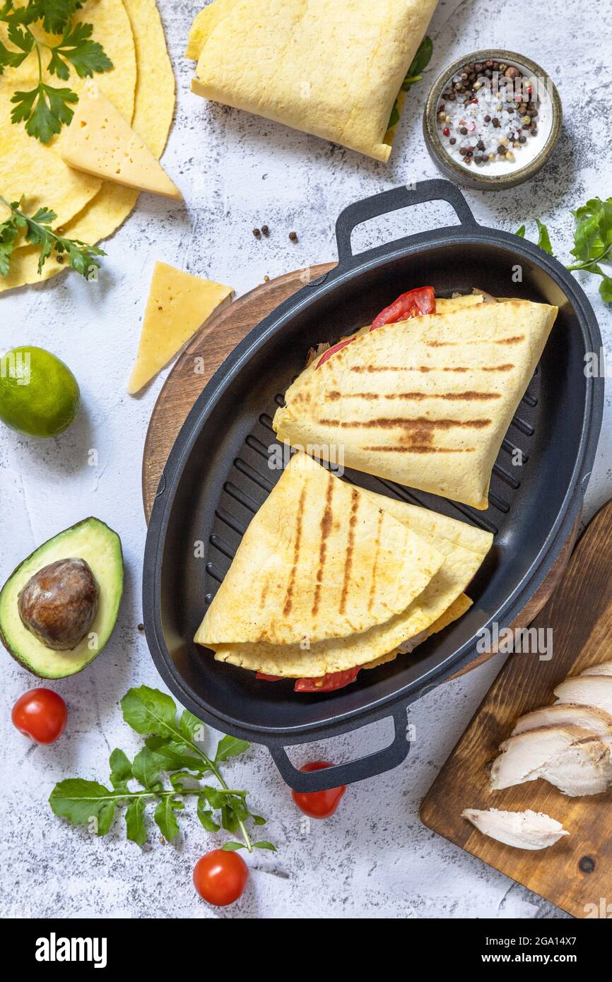 Mexikanisches Sandwich-Hühnchen-Maistortillas mit Avocado, Rucola und Käse auf einer Tischplatte aus grauem Stein. Draufsicht flach lay Hintergrund. Stockfoto