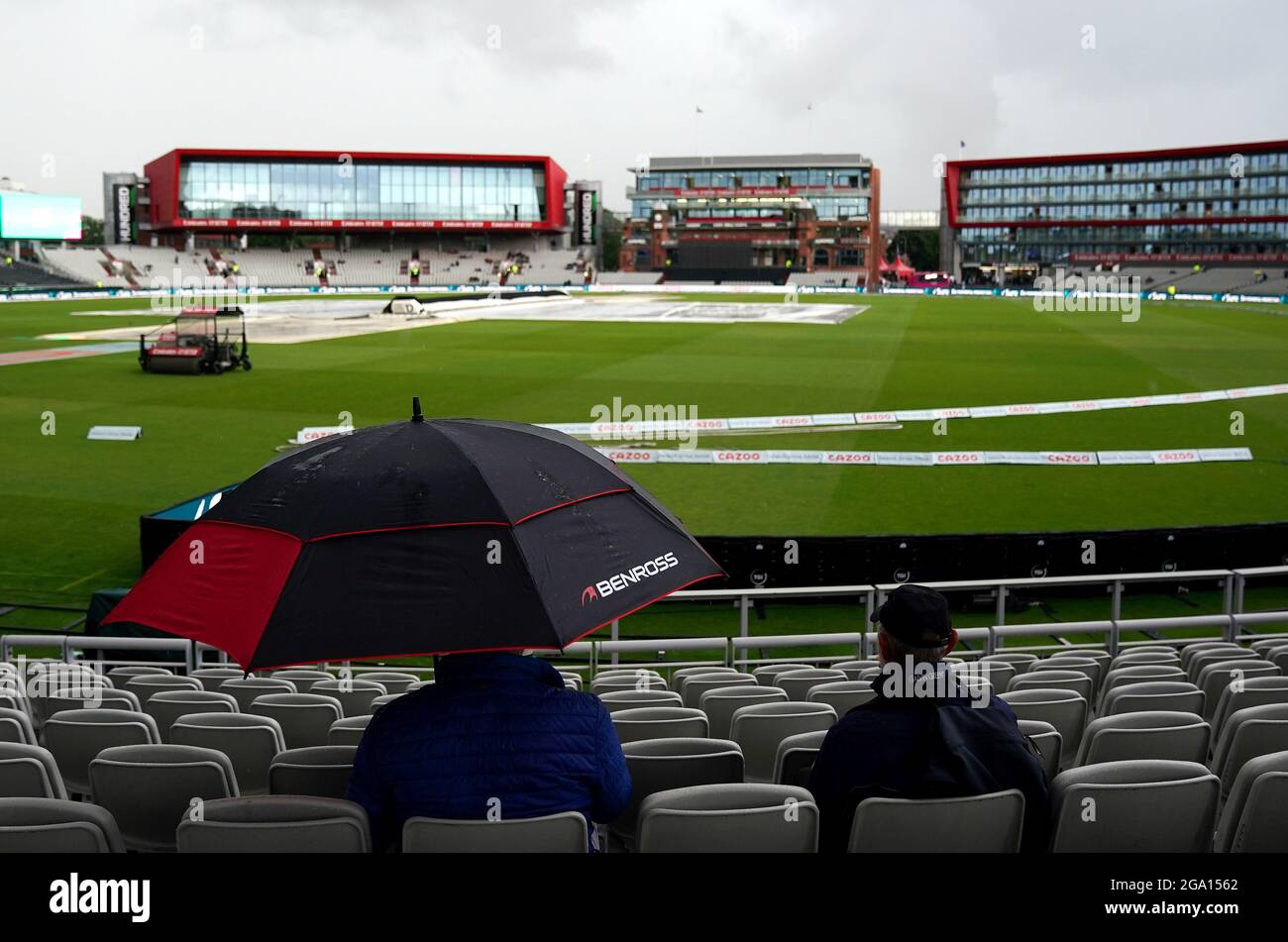 Die Zuschauer halten sich unter einem Regenschirm zurück, während der Regen den Beginn des Spiels während des 100-Matches im Emirates Old Trafford, Manchester, verzögert. Bilddatum: Mittwoch, 28. Juli 2021. Stockfoto