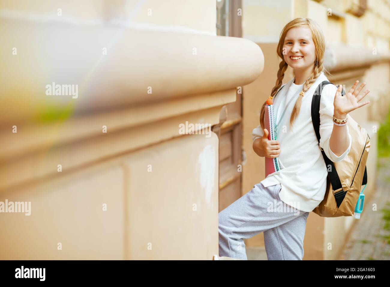 Happy stylish Kind in weißem Sweatshirt mit Arbeitsbuch, Desinfektionsmittel  und Rucksack Hand winken und gehen zur Schule im Freien in der Stadt  Stockfotografie - Alamy