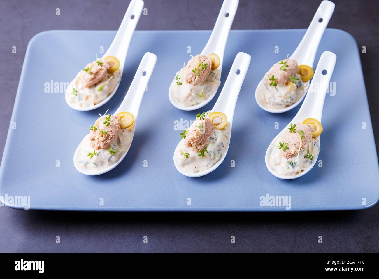 Kalte Vorspeise aus Kabeljauleber, Kabeljaukaviar, Oliven, Gurken und Mikrogemüse auf Servierlöffeln. Traditionelle kalte Gerichte. Nahaufnahme, blaue Platte, schwarz Stockfoto