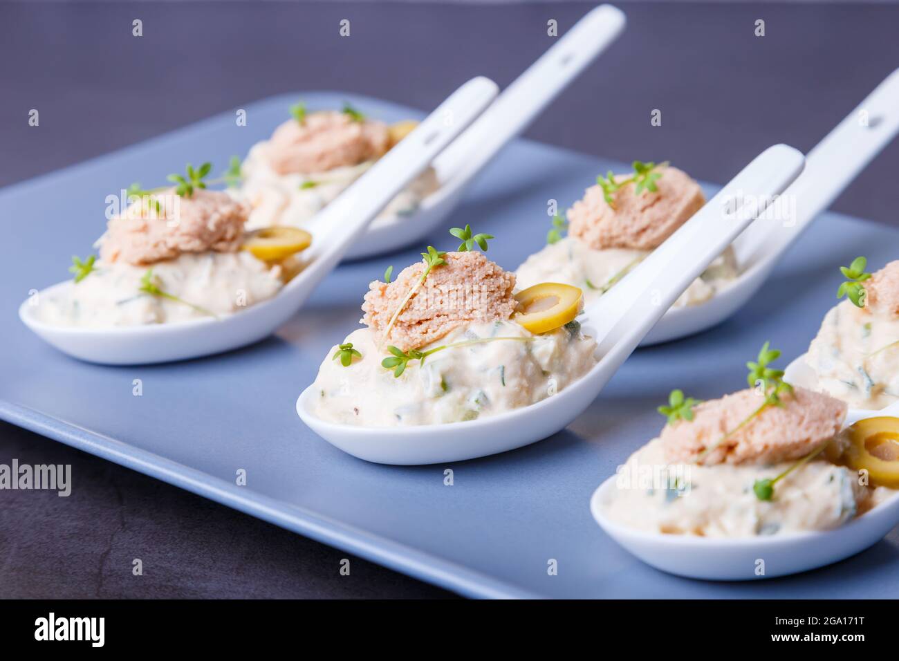 Kalte Vorspeise aus Kabeljauleber, Kabeljaukaviar, Oliven, Gurken und Mikrogemüse auf Servierlöffeln. Traditionelle kalte Gerichte. Nahaufnahme, blaue Platte, schwarz Stockfoto