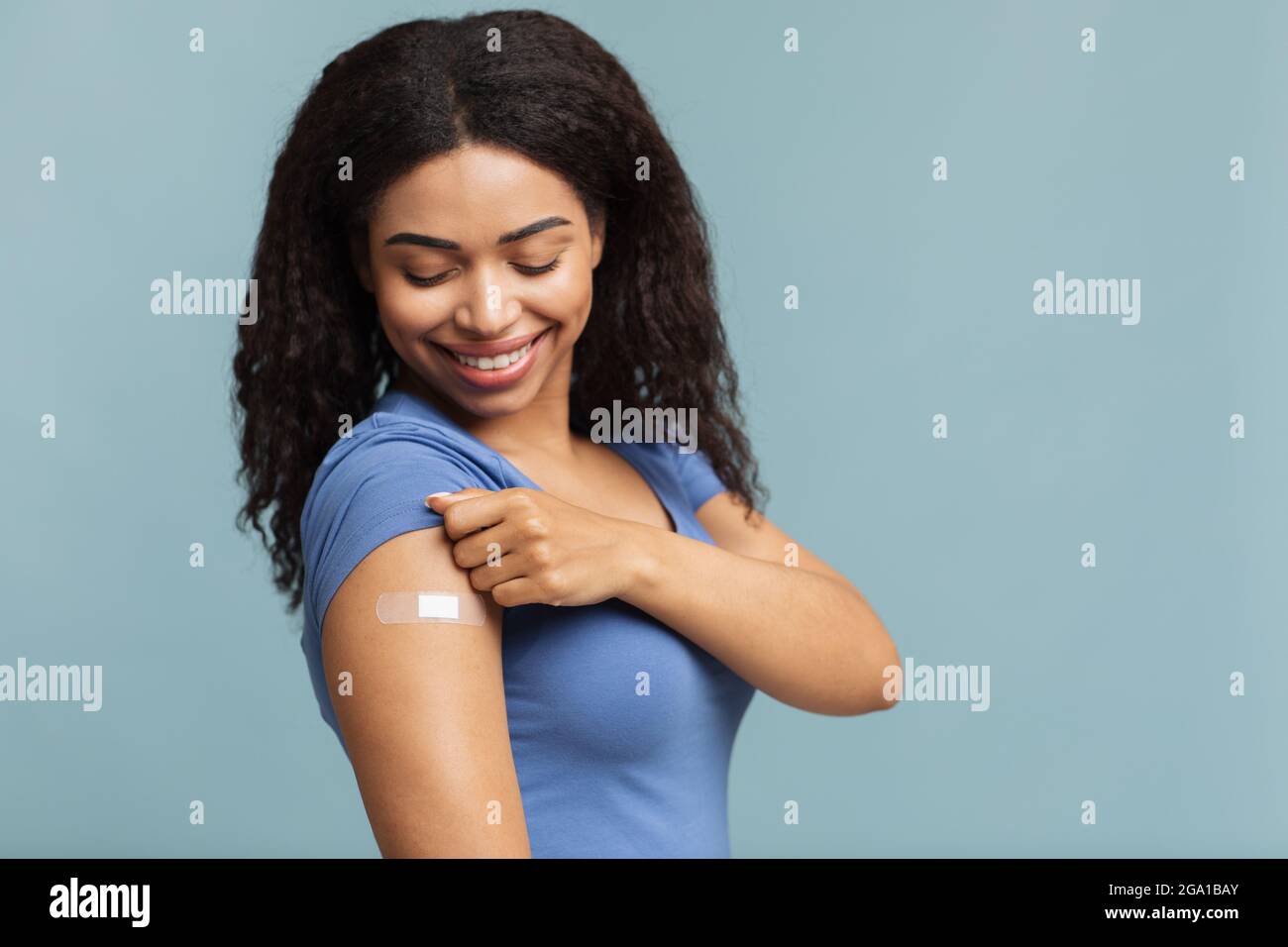 Werbung für die Impfung gegen Coronaviren. Glücklich geimpfte schwarze Dame zeigt Arm mit Gips auf blauem Hintergrund Stockfoto