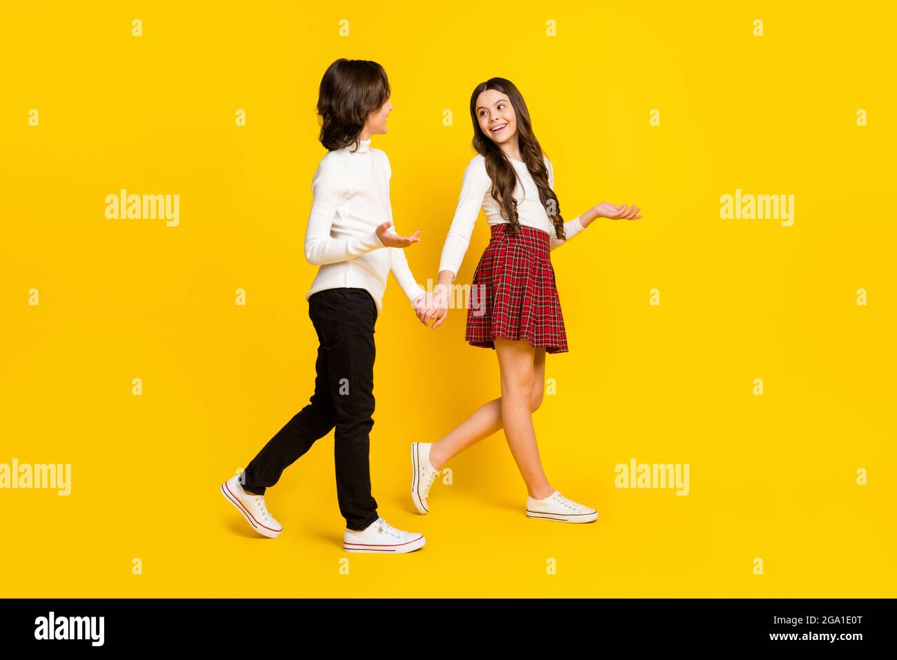 In voller Länge Körpergröße Seitenprofil Foto von Kindern halten Hände gehen miteinander sprechen isoliert leuchtend gelben Hintergrund Stockfoto
