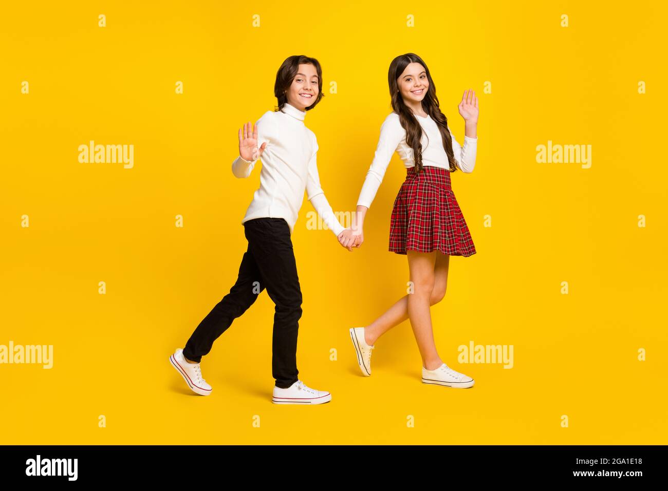 In voller Länge Körpergröße Seitenprofil Foto von Kindern halten Hände gehen zur Schule winkende Hände isoliert lebendige gelbe Farbe Hintergrund Stockfoto