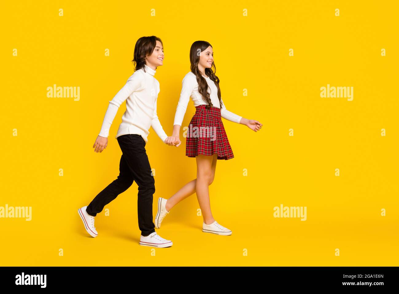 In voller Länge Körpergröße Seitenprofil Foto von Kindern lächelnd halten Hände gehen zur Schule isoliert lebendige gelbe Farbe Hintergrund Stockfoto