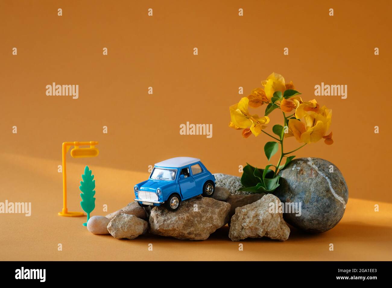 Blaues Spielzeugauto auf Steinen und orangefarbenem Hintergrund wie ein Symbol für Roadtrips.Reisekonzept oder Autovermietung. Stockfoto