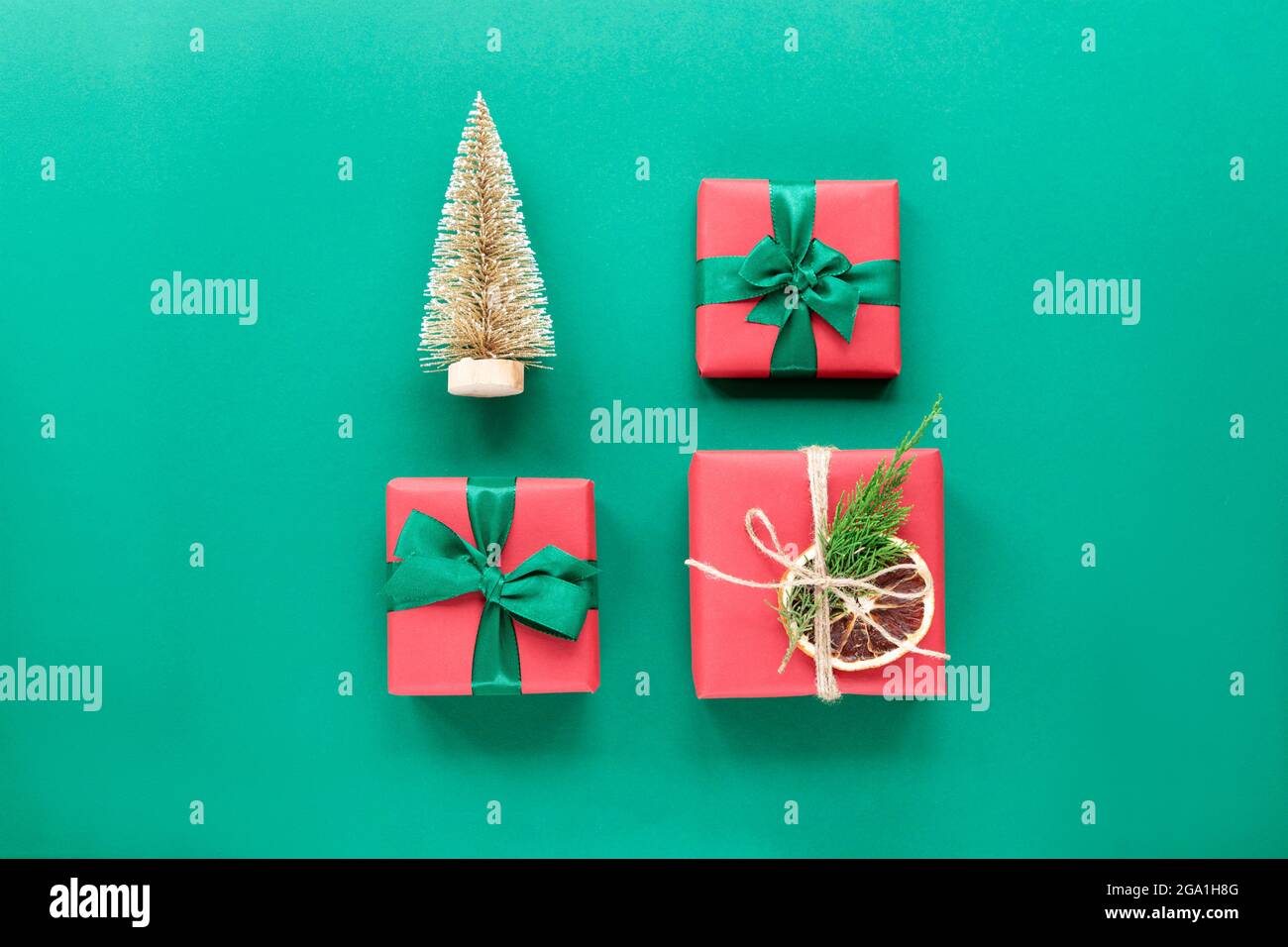 Drei Weihnachtsgeschenke und dekorative Tannenbäume in ordentlichen Reihen auf grünem Hintergrund. Festliches Neujahrskonzept. Draufsicht, flach liegend. Stockfoto