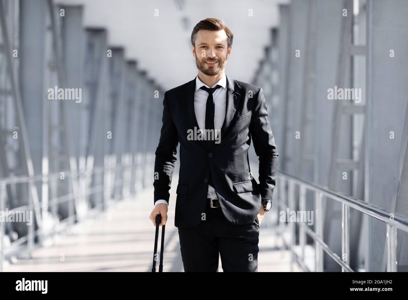 Wohlhabender Manager in schwarzem Anzug mit Koffer im Flughafen Stockfoto
