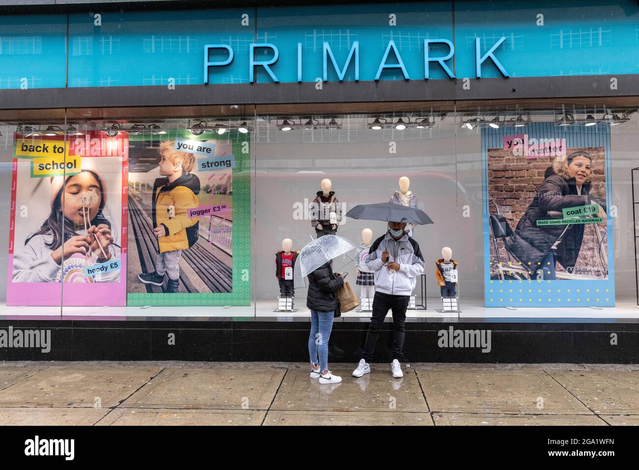 Bei den starken Regenschauern im Juli 2021 in London, England, Großbritannien, stehen die Käufer vor einer Filiale von „Primark“ in der Oxford Street unter Regenschirmen Stockfoto
