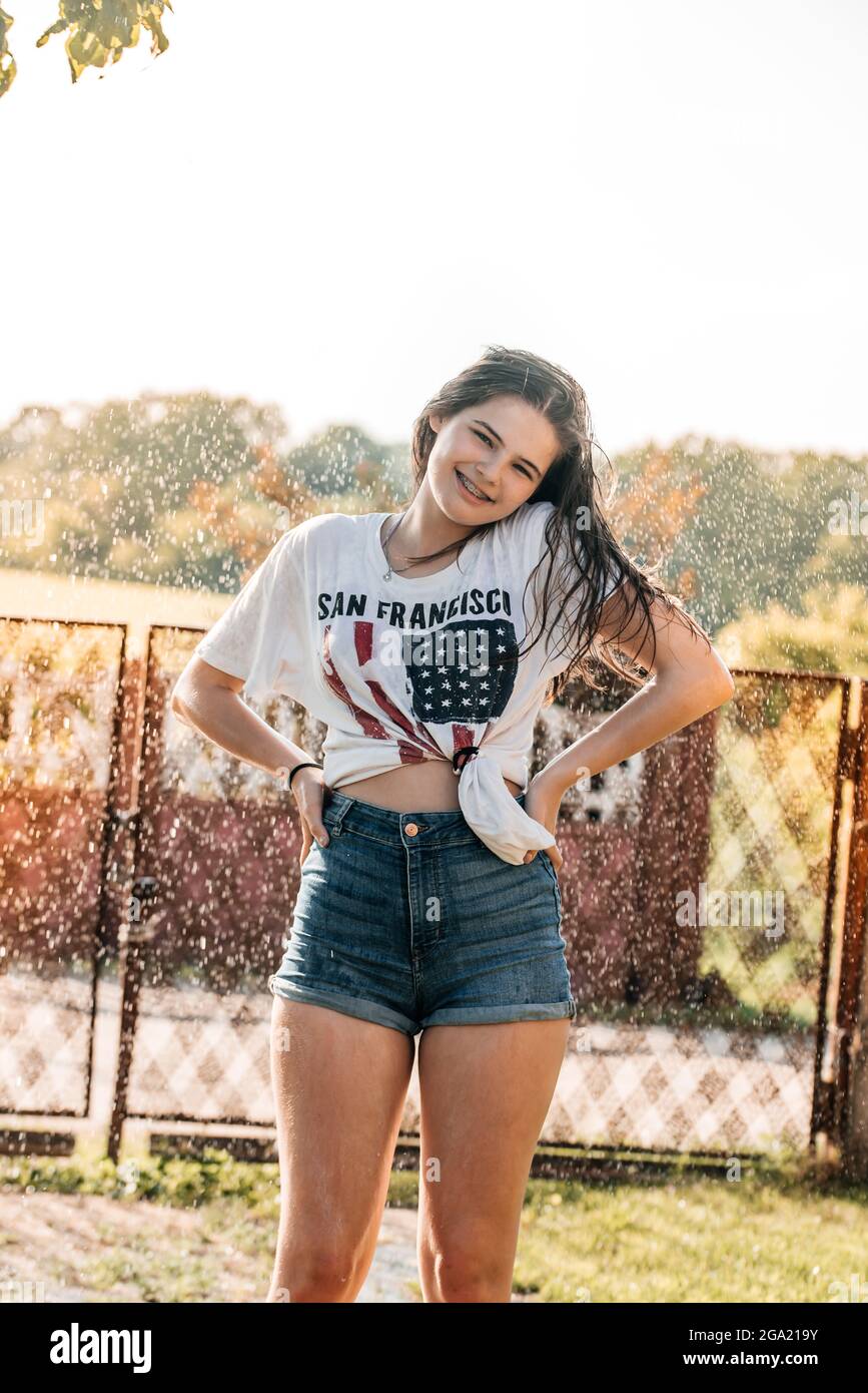 Mädchen mit einem Brunnen im Garten bei Sonnenuntergang. Heißer Sommer, nasses Hemd. USA-Flagge Stockfoto