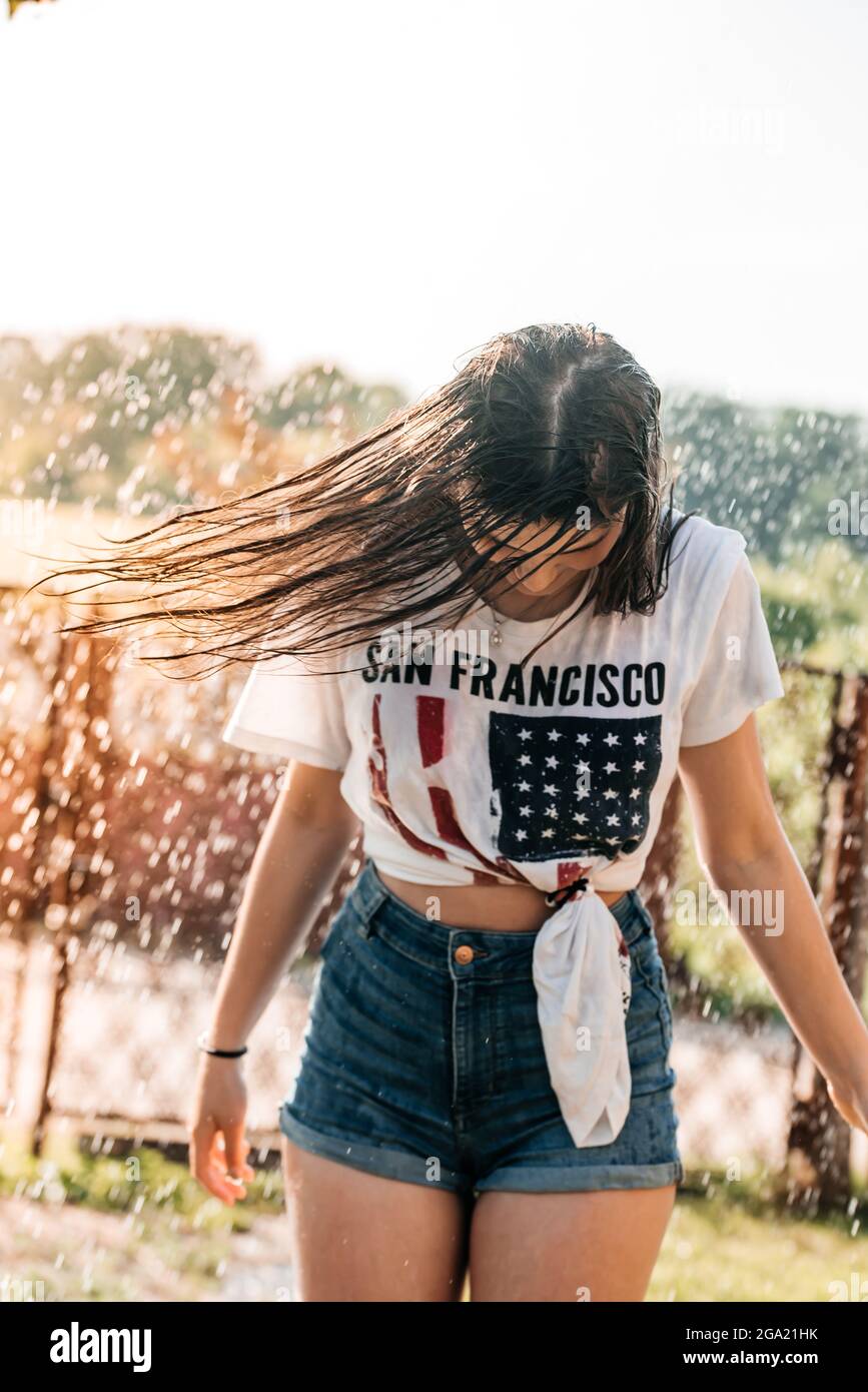 Mädchen mit einem Brunnen im Garten bei Sonnenuntergang. Heißer Sommer, nasses Hemd. USA-Flagge Stockfoto