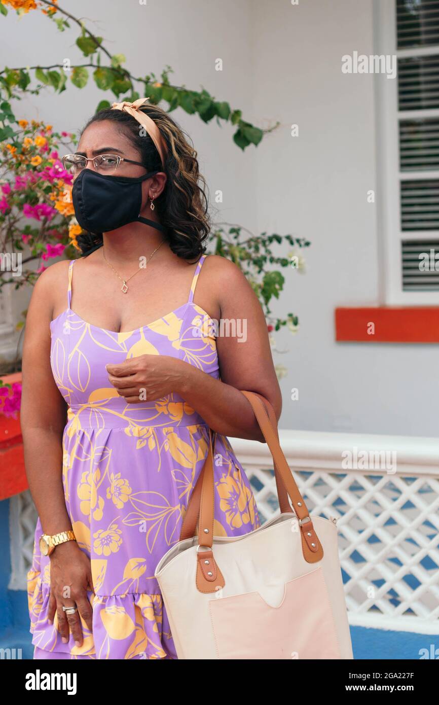 Schönes Mädchen mit einer Virenschutzmaske und einem Sommerkleid, das allein auf einer Straße posiert Stockfoto