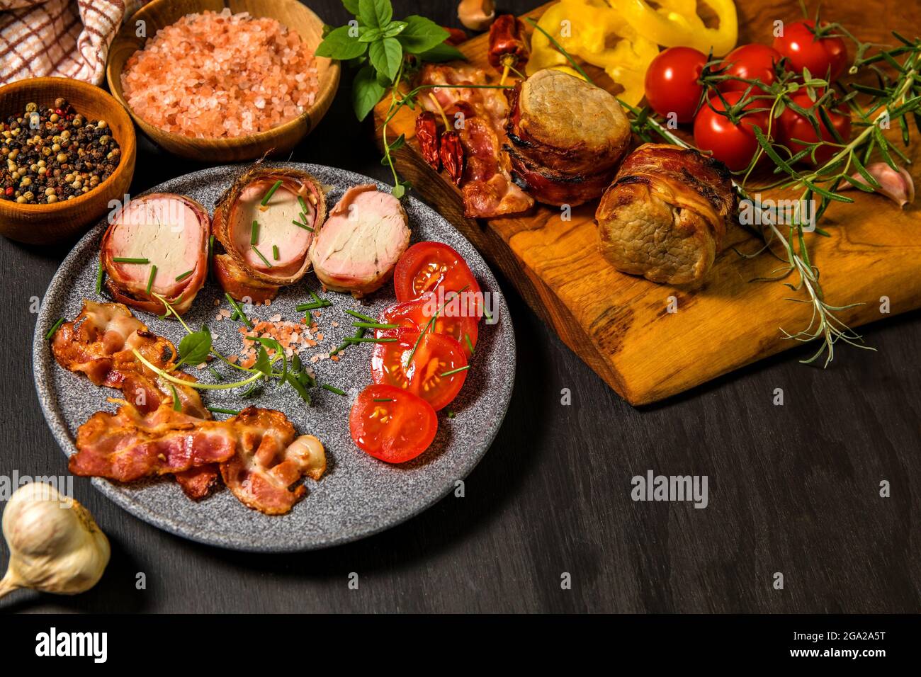 Gegrillte Schweinemedaillons mit Kräutern und Gewürzen. Schweinelende mit Speck. Gegrilltes Fleisch und Tomaten. Sommergrill. Stockfoto