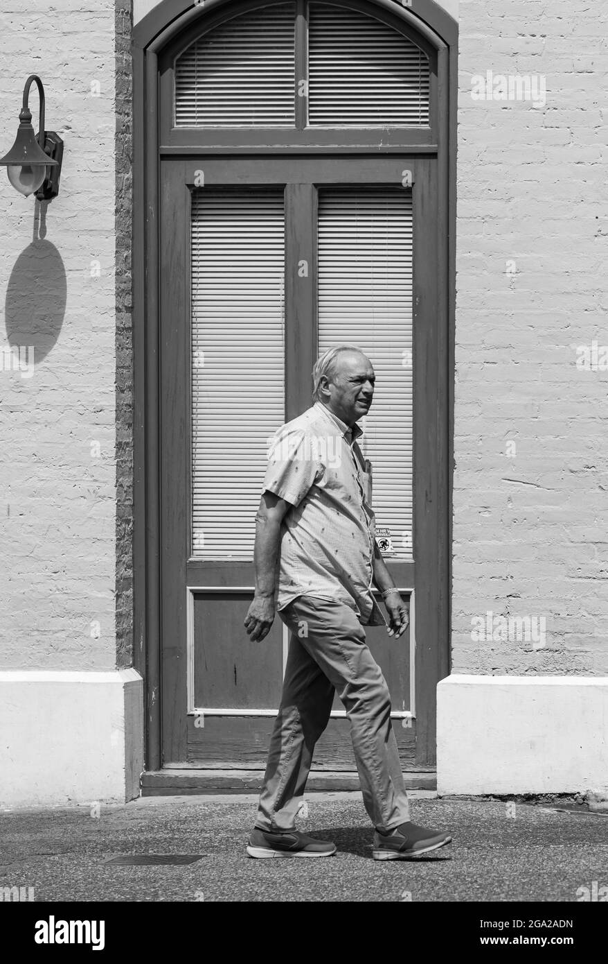 Ein alter Mann geht auf einem Bürgersteig im Hintergrund der Tür des Gebäudes. Schwarz-Weiß-Foto im Vintage-Stil. Victoria, BC, Kanada – Juli 23,2021. Stockfoto