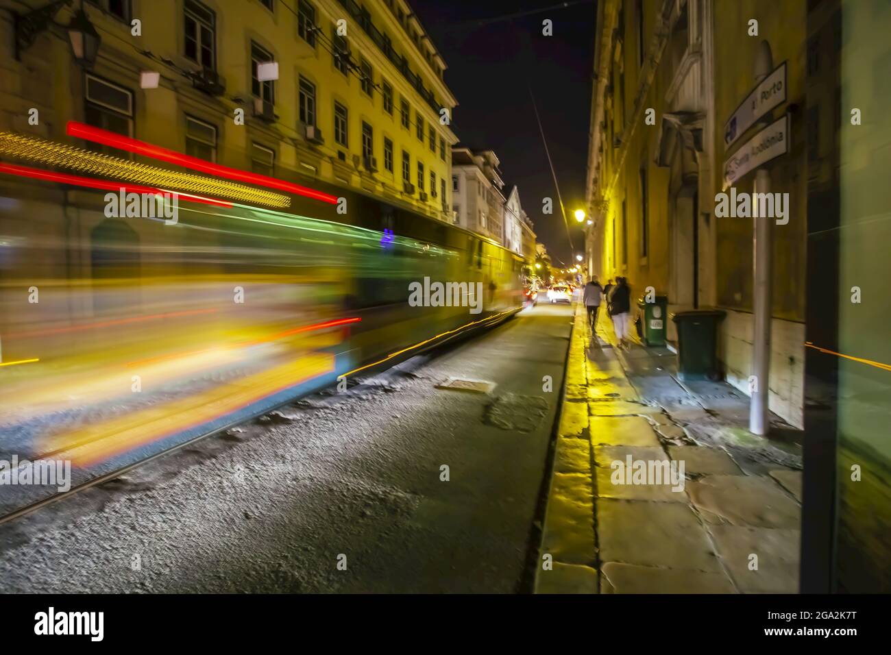 Verschwommene Straßenbahn, die nachts durch die kopfsteingepflasterten Straßen der historischen Stadt Lissabon fährt; Lissabon, Lissabon, Portugal Stockfoto