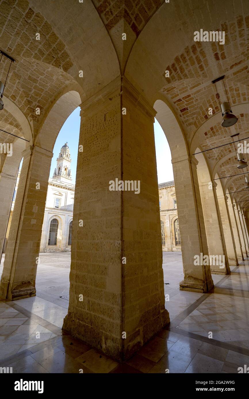 Blick auf den Glockenturm der Kathedrale von Lecce durch Säulen unter dem Portikus vor den Gebäuden rund um die Piazza del Duomo in Lecce Stockfoto