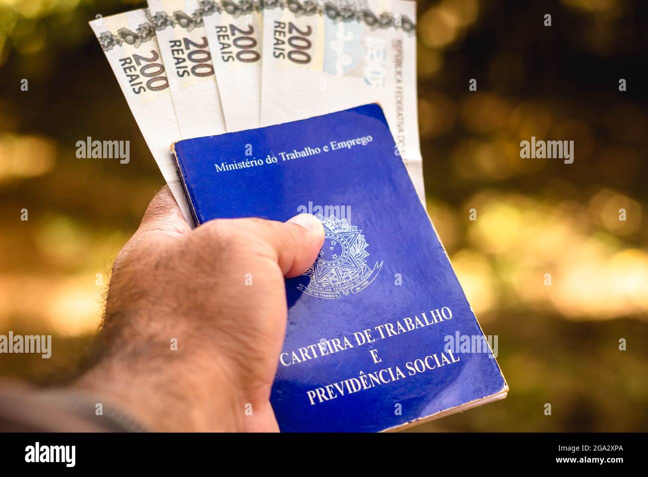 In dieser Fotolabbildung zeigt ein Mann seine Arbeits- und Sozialversicherungskarte Brasiliens mit zweihundert Reals-Rechnungen, das Dokument, das den Zugang zu den Rechten des brasilianischen Arbeiters garantiert. Stockfoto