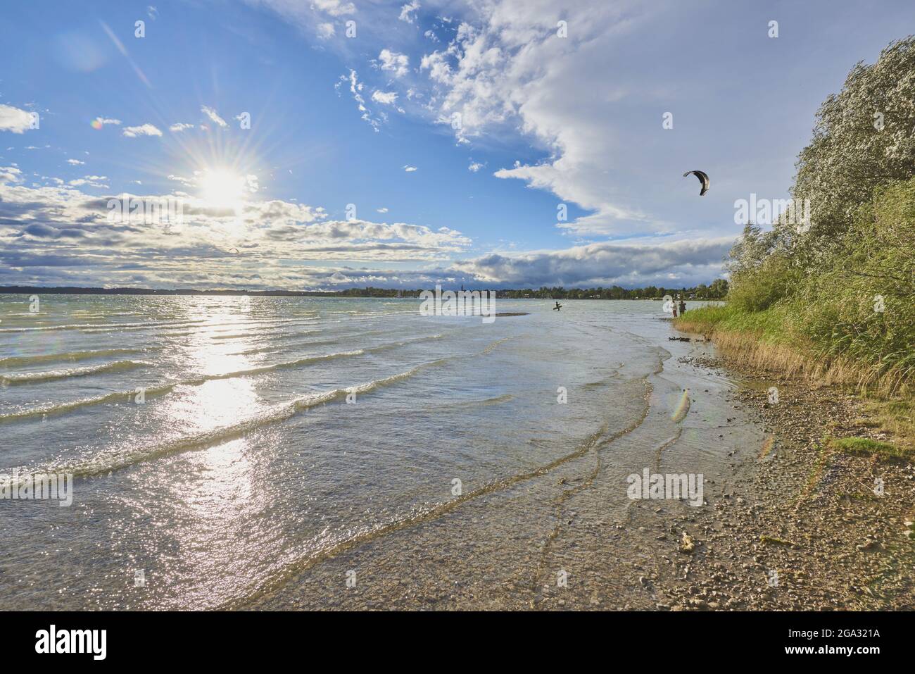 Chiemsee, mit hellem Sonnenlicht auf der Wasseroberfläche reflektiert und ein Kitesurfer in der Nähe des Ufers; Bayern, Deutschland Stockfoto