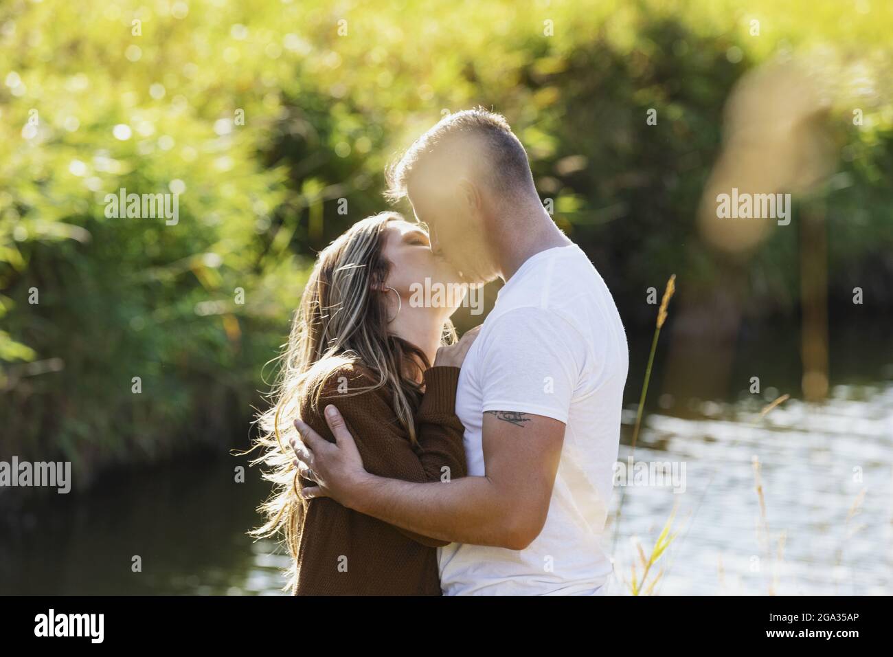Ehemann und Ehefrau verbringen viel Zeit miteinander und küssen sich im Freien in der Nähe eines Baches in einem Stadtpark; Edmonton, Alberta, Kanada Stockfoto