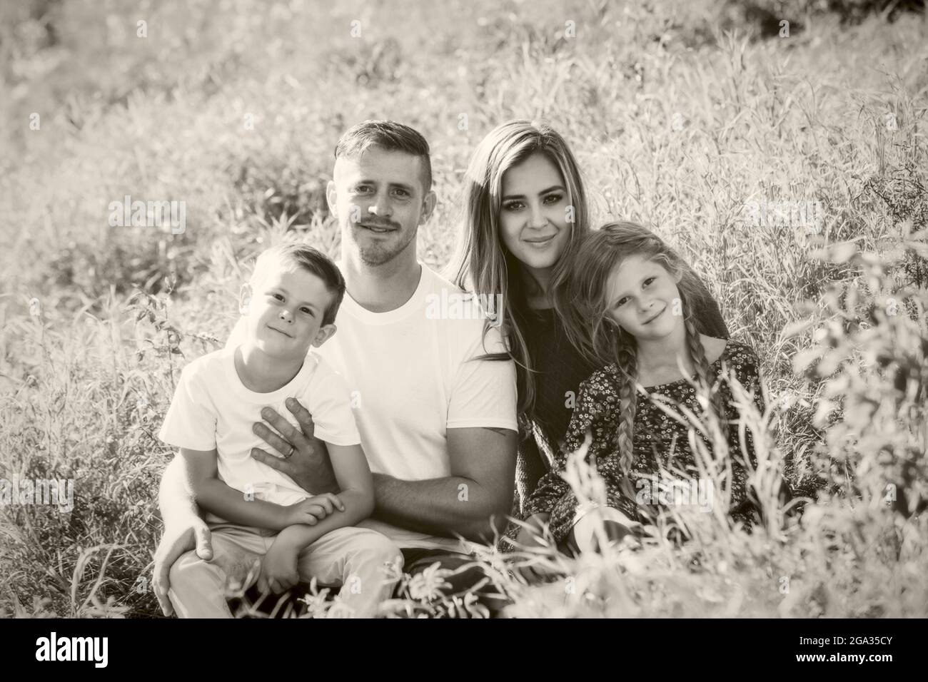 Schwarz-Weiß-Porträt einer vierköpfigen Familie mit zwei kleinen Kindern, die auf Gras in einem Park sitzen; Edmonton, Alberta, Kanada Stockfoto