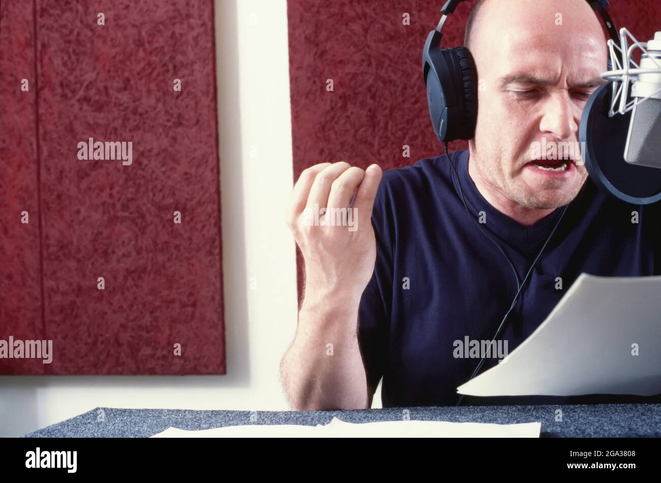 Mann, der in einem Aufnahmestudio in einem Mikrofon liest; Studio Stockfoto