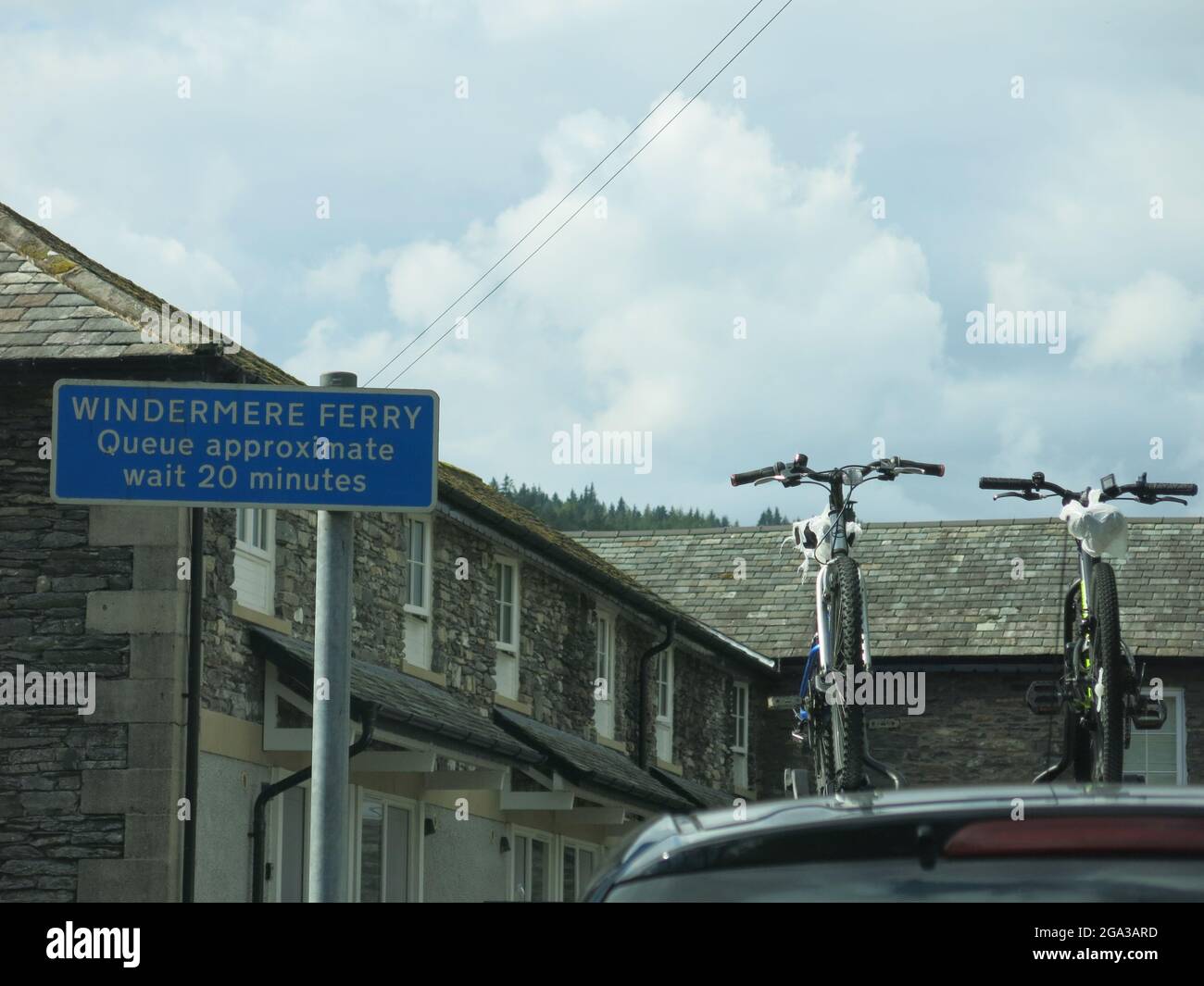 Radurlaub im Lake District: Foto von zwei Fahrrädern auf einer Autodachstange, während sie in der Warteschlange am 20 Minuten langen Schild für die Autofähre stehen. Stockfoto