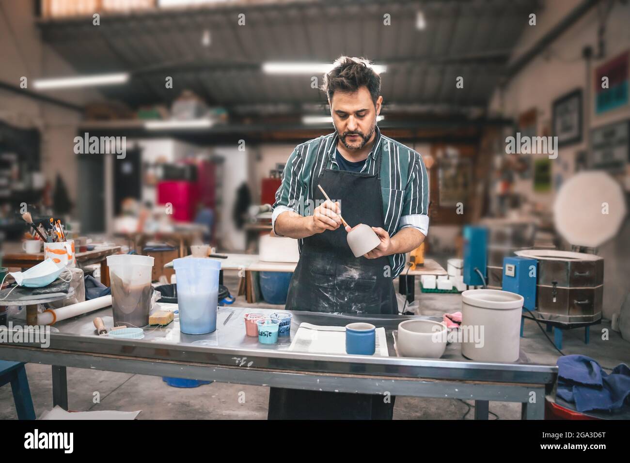 Ein erwachsener hispanischer Mann malt in einer Werkstatt einen Tontopf über einem Tisch Stockfoto