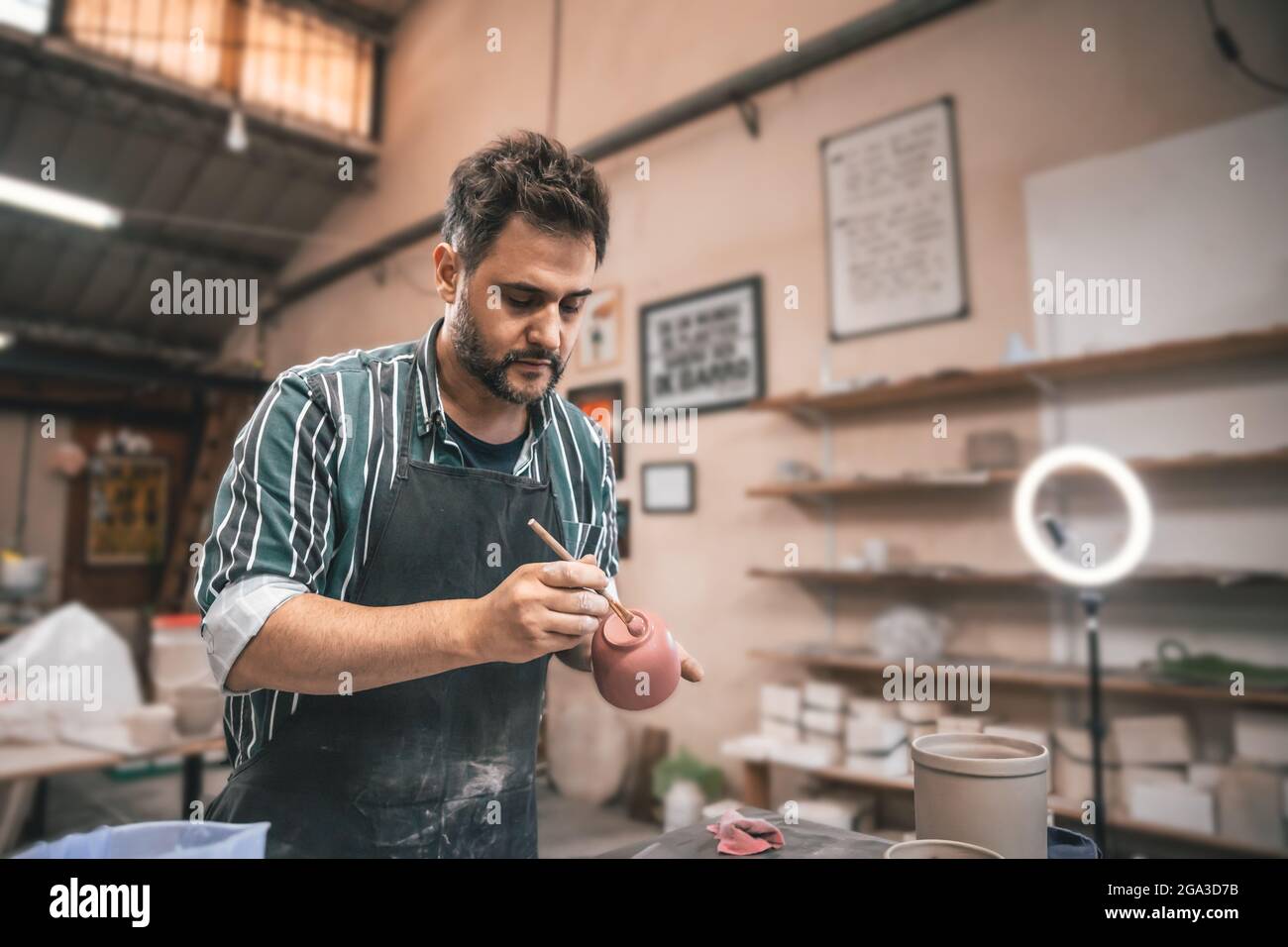Ein erwachsener hispanischer Mann malt in einer Werkstatt einen Tontopf über einem Tisch Stockfoto