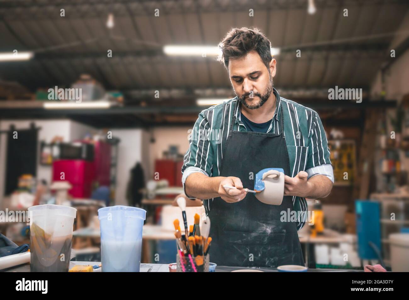Ein erwachsener hispanischer Mann malt in einer Werkstatt einen Tontopf über einem Tisch Stockfoto
