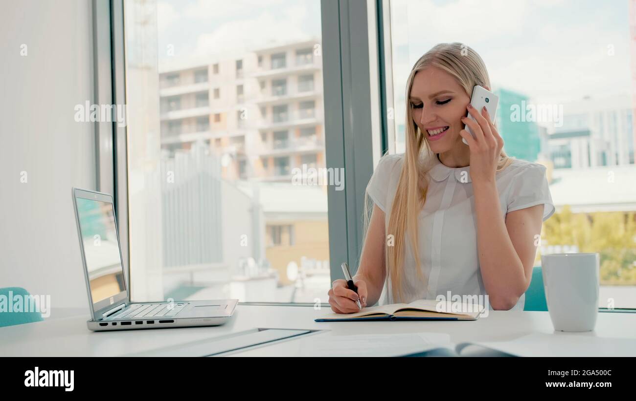 Elegante, moderne Geschäftsfrau mit Laptop und Papieren am langen Tisch im Konferenzraum mit Telefonanruf Stockfoto