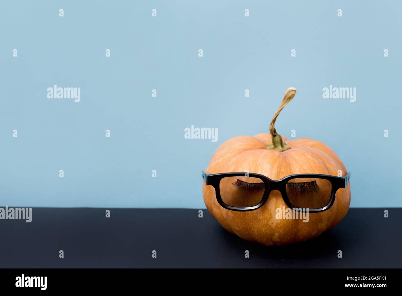 Kürbis mit falschen Wimpern und Sonnenbrille auf blauem Hintergrund, Halloween Stockfoto