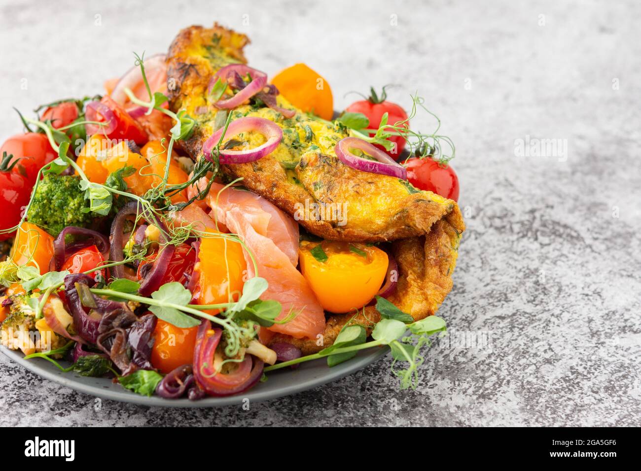 Omelette mit geschmortem Gemüse und Lachs, Tomaten mit Zwiebeln, Brokkoli und rotem Fisch mit Erbsen-Microgreens, leckeres herzhaftes Frühstück Stockfoto