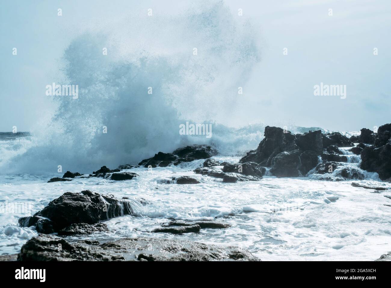 Eine mächtige Meereswelle spritzt über einen großen Felsen mitten in der rauen See. Stockfoto