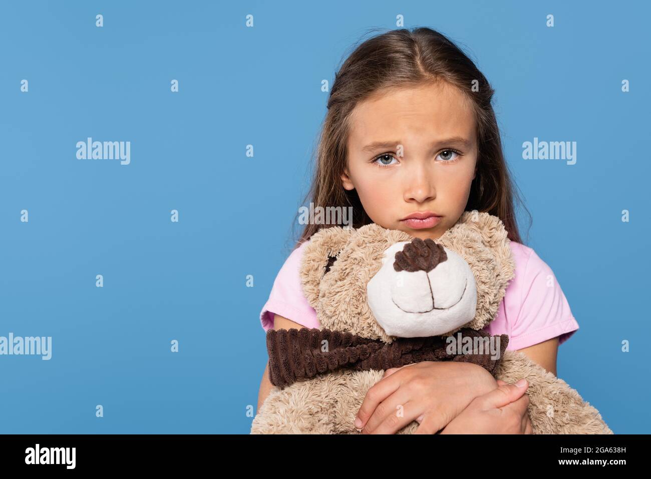 Trauriges Mädchen, das weiches Spielzeug hält und die Kamera isoliert auf Blau anschaut Stockfoto