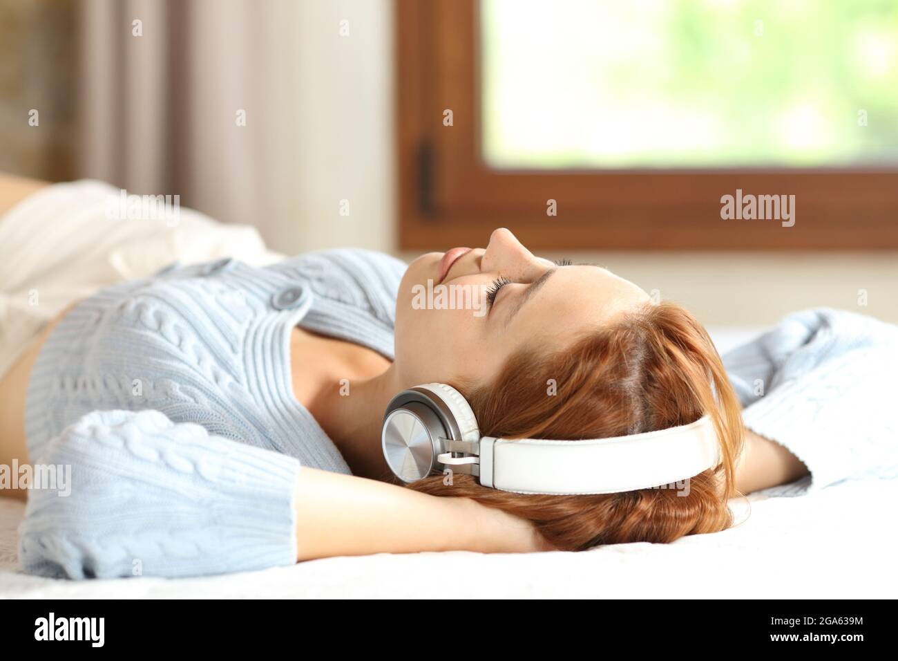 Entspannte Frau, die sich auf einem Bett ausruhte und Musik mit kabellosen Kopfhörern zu Hause hörte Stockfoto