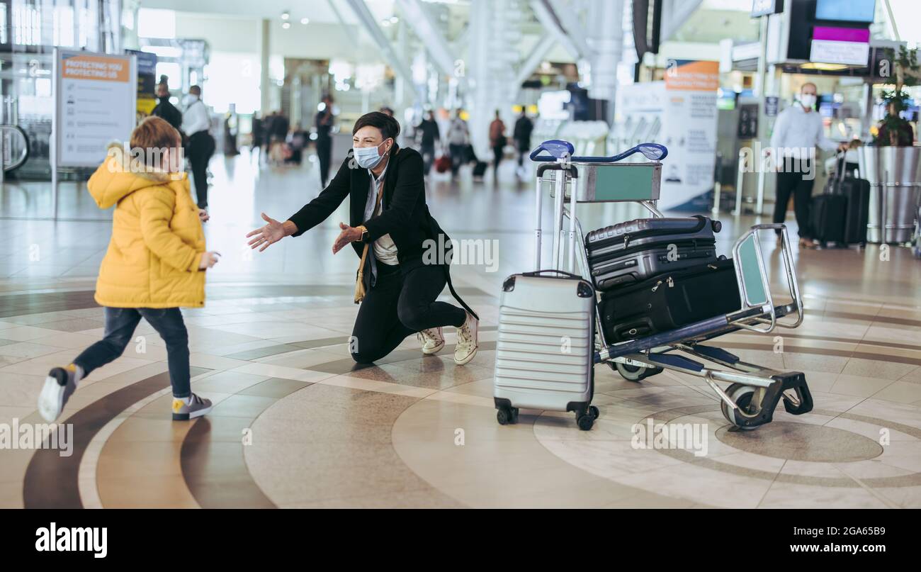 Kleiner Junge, der während einer Pandemie auf seine Mutter zuläuft und nach einer Reise am Flughafen ankommt. Sohn trifft Mutter bei der Ankunft am Flughafen. Stockfoto