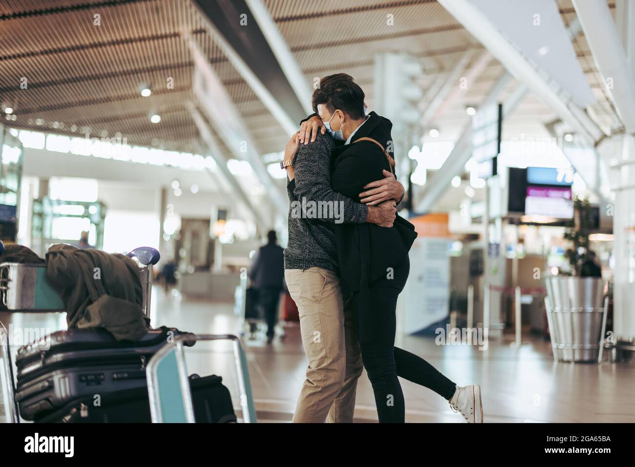 Liebevolles Paar, das sich während des Treffens am Flughafen umarmte, nachdem der Mann von der Reise zurückkehrte. Frau umarmte Mann nach der Ankunft von Reise während einer Pandemie. Stockfoto