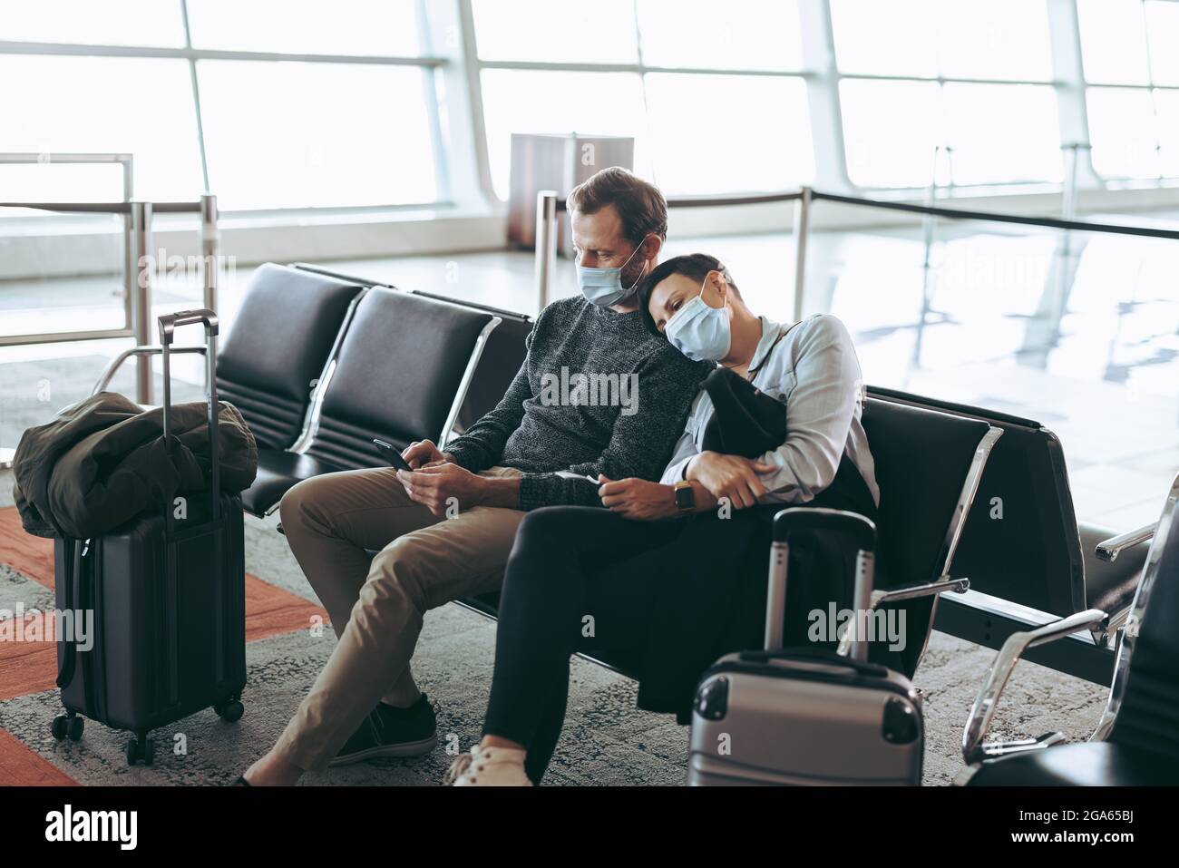 Reisenpaar in Pandemie wartet am Flughafenterminal. Mann und Frau in Gesichtsmasken sitzen im Wartebereich am Flughafen. Stockfoto