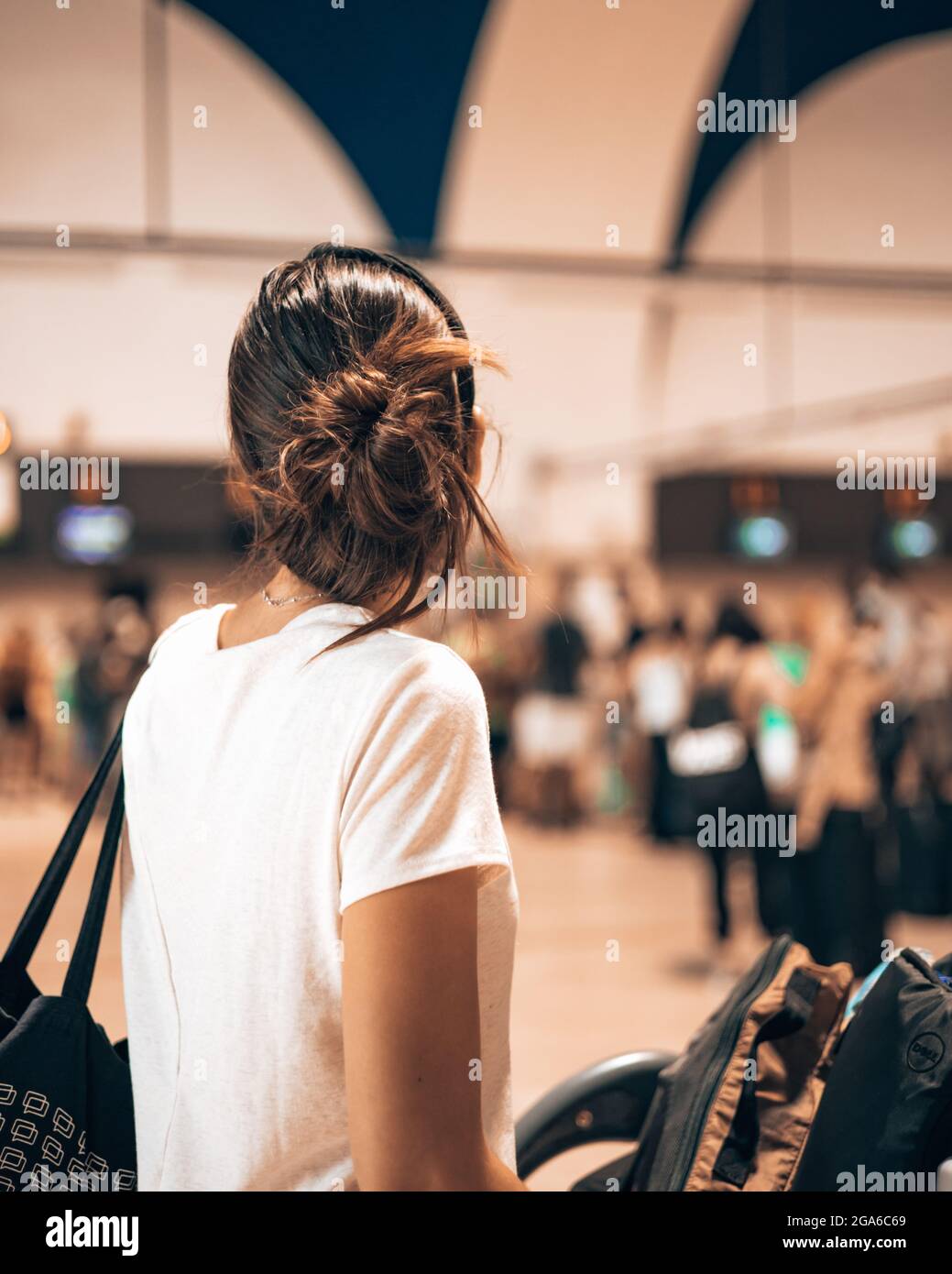 Kaukasische Frau, die während der aufsehenbaren Pandemie in den Flughafenterminal ging und ihr Gepäck auf einen Trolley lad, während sie die lange Schlange beim Check-in beobachtete Stockfoto