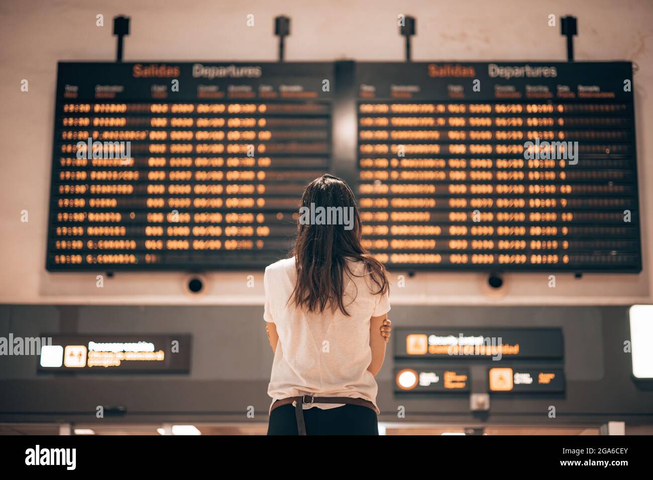 Frau in einem Flughafenterminal, die auf die großen Bildschirme schaut, die die Abflug- und Ankunftszeiten der Flugzeuge zeigen, und auf die Details ihres Fluges wartet Stockfoto