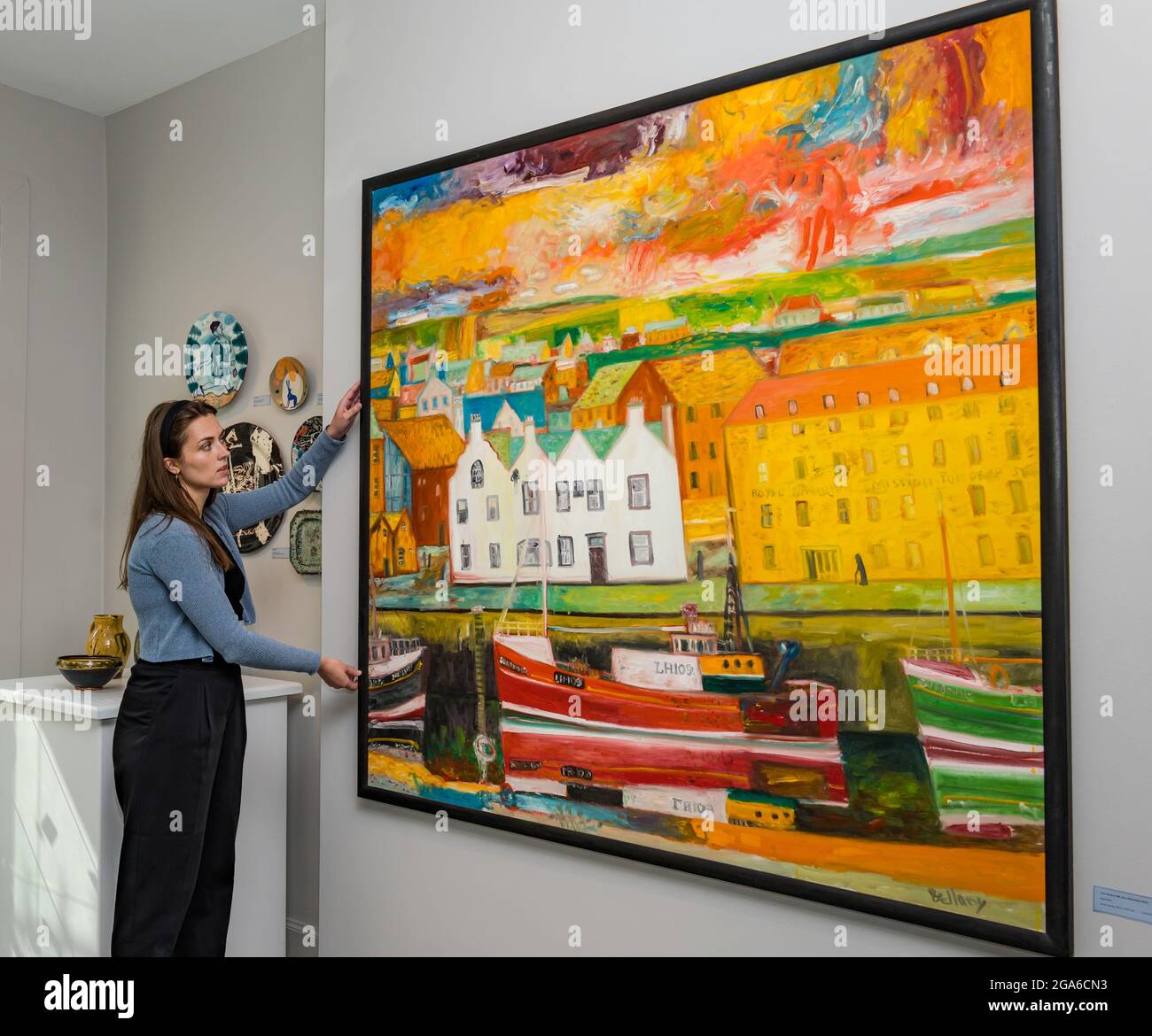 The Scottish Gallery, Edinburgh, Schottland, Großbritannien, 29. Juli 2021. Edinburgh Art Festival: Im Bild: Amy, Praktikantin in der Scottish Gallery, mit einem John Bellany Gemälde von Eyemouth, Teil der J G Scott Sammlung Stockfoto