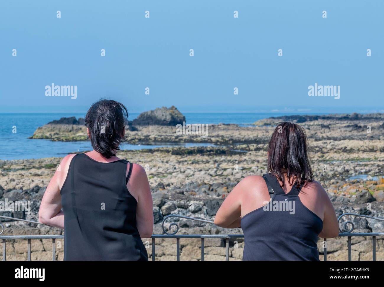 Zwei Freundinnen am Meer mit Blick auf das Wasser plaudern im Dunure Harbour in ayrshire an der schottischen Küste. Stockfoto