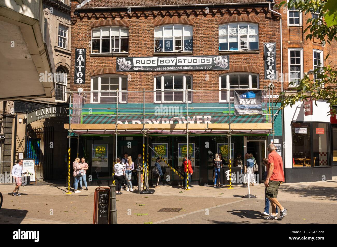 Orford Place Norwich City Centre Paddy Power Buchmacher mit Rudeboy Studios und einem Tattoo- und Piercing-Shop mit Menschen, die draußen für Piercings Schlange stehen. Stockfoto