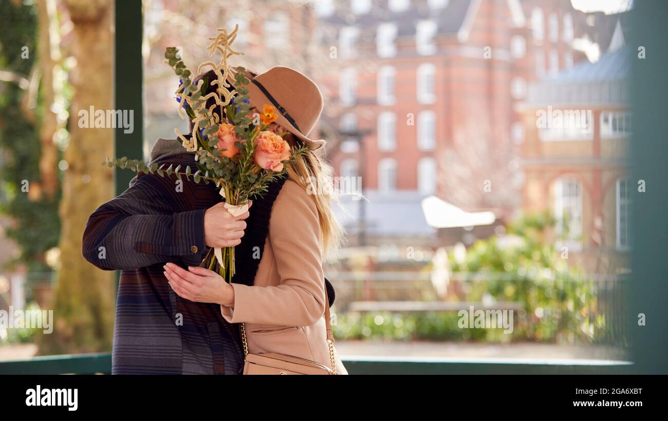 Romantischer Mann umarmt junge Frau mit Gesichtern versteckt hinter EINEM Blumenstrauß gibt er ihr Stockfoto