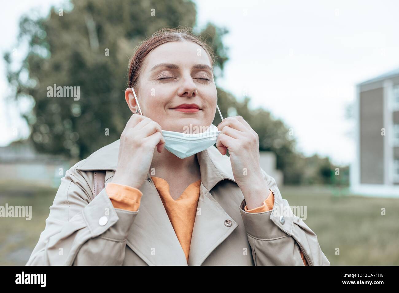 Frau, die an einem sonnigen Tag die Maske auszieht, um frische Luft auf der Straße zu atmen Stockfoto